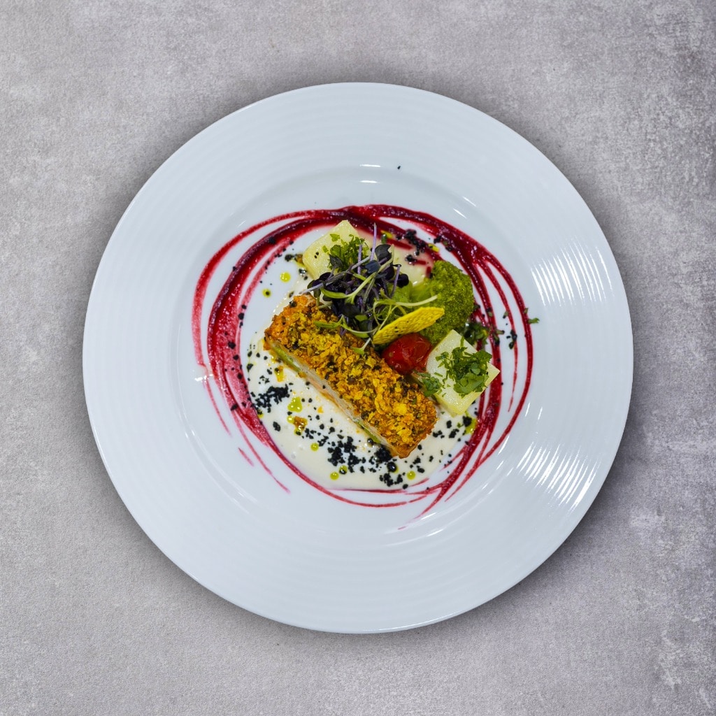 Ruladă de șalău aromatizat cu pesto roșu, în crustă de porumb și alune, servită cu sos de usturoi și garnitură de broccoli, roșii cherry sote și cartofi natur