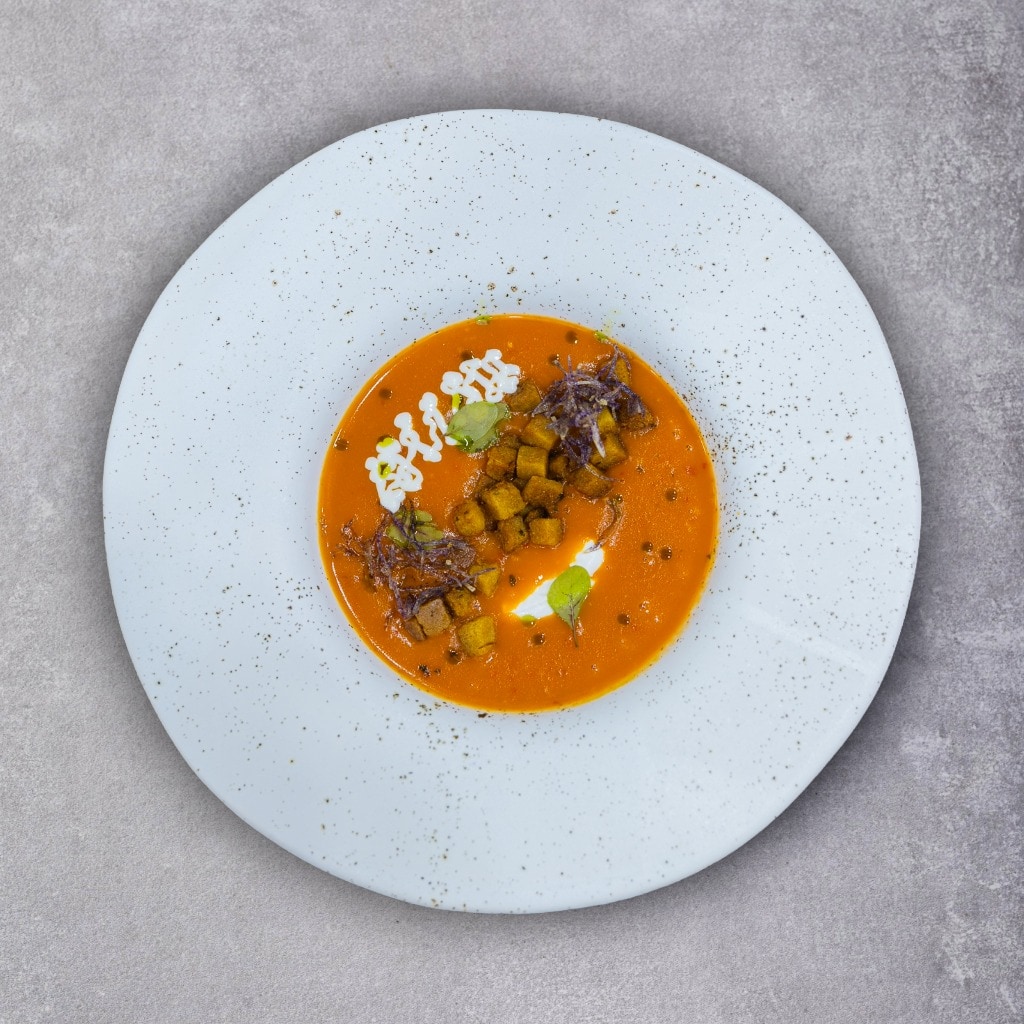 Supă cremă de roșii cu ardei copți servită cu quenelle de brânză de capră și crutoane aromatizate cu busuioc